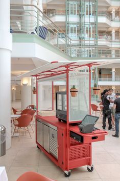 a red cart with a tv on top of it in a lobby next to tables and chairs