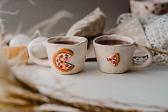 two coffee mugs with designs on them sitting on a table next to some pillows