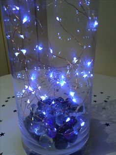 a vase filled with lots of blue glass rocks and lights on top of a table