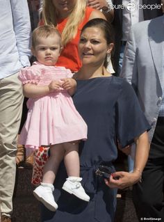 a woman holding a baby in her arms and smiling at the camera with other people behind her