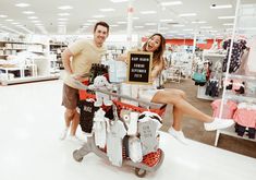 a man and woman sitting on top of a shopping cart in a store