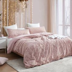 a bed with pink comforter and pillows in a bedroom next to a chandelier