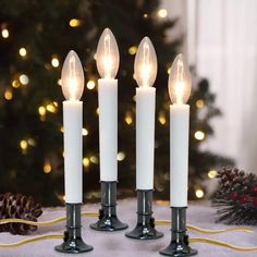 three white candles sitting on top of a table next to a christmas tree with lights