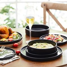 a table topped with black plates and bowls filled with food next to a glass of wine