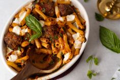 a pasta dish with meatballs and cheese in a white bowl next to a wooden spoon