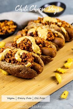 baked chili cheese dogs on a wooden cutting board with other food items in the background