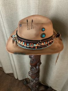 This is a custom weathered hat with incredible detail.  Tan felt with western fabric of orange, turquoise, black and white.  Strand of turquoise beads.  Black and brown hat band with silver studs, silver bull and raw hide ties.  Jute tied around.  Black safety pins.  Turquoise embellishments.  Turquoise stitching on edge.  Adjustable band inside to fit any size. Rustic Festival Hat Bands For Short Brim Hats, Rustic Adjustable Felt Hat For Festival, Rustic Brown Hat For Festival, Southwestern Brown Felt Hat For Rodeo, Rustic Handmade Hat Bands For Rodeo, Southwestern Brown Felt Hat For Western-themed Events, Handmade Rustic Hat Bands For Rodeo, Handmade Rustic Rodeo Hat Bands, Handmade Rustic Hat Band For Festivals