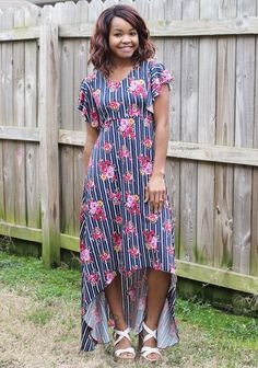 a woman standing in front of a wooden fence wearing a dress with flowers on it