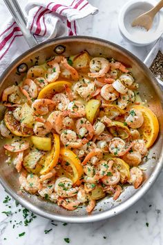 a pan filled with shrimp and lemons on top of a white marble countertop