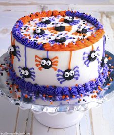 a decorated cake with orange and purple icing on a plate, sitting on a wooden table