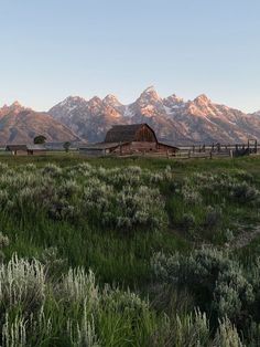 an old barn in the middle of a field with mountains in the background