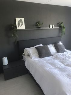 a large bed with white sheets and pillows in a dark colored room, along with two planters on the wall