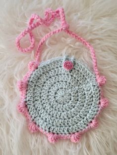 a crocheted purse with a pink flower on the front and bottom, sitting on a white fur surface