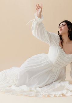 a woman in a white dress sitting on the floor with her hands up and arms outstretched