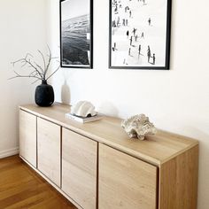 two framed pictures hang on the wall above a wooden cabinet in a room with hard wood floors