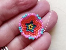 someone is holding a beaded brooch in their left hand and it looks like they are making something out of beads