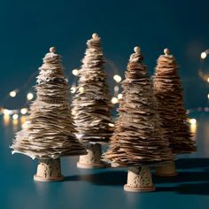 three small christmas trees made out of old newspapers and string lights on a blue background