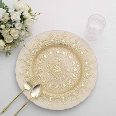 a white plate with gold trim and two silver spoons on it next to flowers