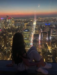 a woman sitting on top of a tall building looking out at the cityscape