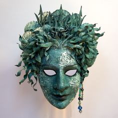 a green mask with leaves and beads hanging from it's sides, on a white wall