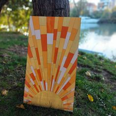 an orange and white piece of art sitting next to a tree in front of a body of water