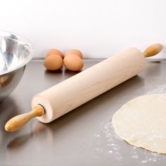 an uncooked pizza dough next to a rolling pin and two eggs on a counter