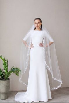 a woman in a white wedding dress and veil standing next to a potted plant