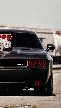 the rear end of a black sports car with red brake lights and an emblem on it