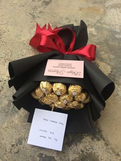 a black and red ribbon wrapped around some chocolates in a gift box with a note attached to it