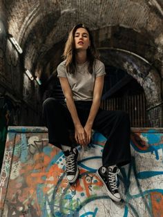 a young woman sitting on top of a skateboard ramp in an abandoned building with graffiti all over the walls