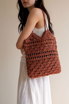 a woman is holding a crocheted brown bag