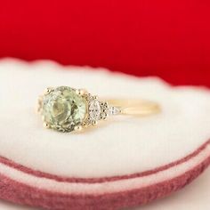 an engagement ring with a green stone and three diamonds on the side, sitting on a cushion