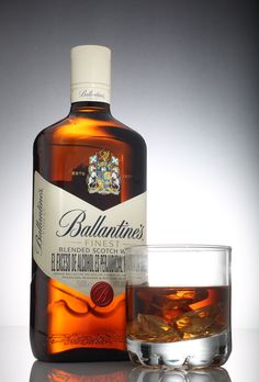 a bottle of ballantines next to a glass filled with liquid and ice cubes