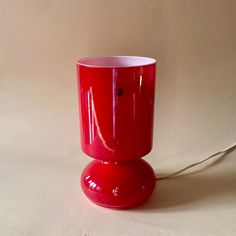 a red cup sitting on top of a table next to a white wall with a cord in it