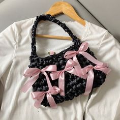 a black and pink handbag hanging from a wooden hanger on a white shirt