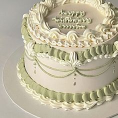 a three tiered cake with white frosting and green trimmings on a plate