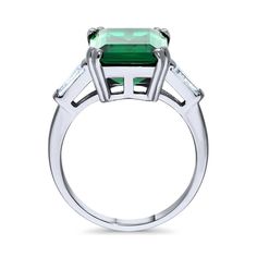 This 3-stone ring makes the ultimate statement with its stunning brilliance and regal high setting. Make a statement and turn heads with this one of a kind beauty. Crafted with fine 925 sterling silver, rhodium plated, nickel free. Main stone features 8.5 carat simulated emerald emerald cut cubic zirconia (14mm x 10mm) in prong setting. Accented with 0.24 ct.tw step-cut trapezoid CZ (5mm x 3mm x 2mm) in bar setting. Ring measures 7.7mm in height. Band measures 2mm in width. Adds a bling on your Fine Jewlery, Jewlery Rings, Cocktail Fashion, Bar Setting, Regal Elegance, Crazy Rich, 3 Stone Rings, Semi Precious Gems, Right Hand Rings