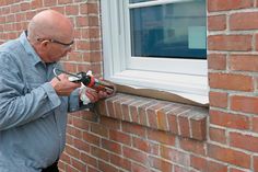 a man is using a power drill to fix a window sealer on a brick wall