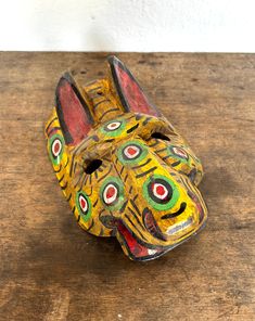 a wooden table topped with a yellow and red animal mask on it's face