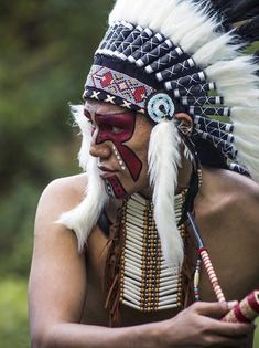 a native american man with his face painted red and white, holding a pipe in his right hand