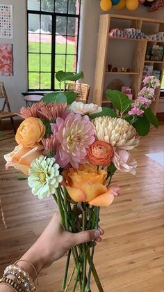 a person holding a bouquet of flowers in their hand on a wooden floor with balloons