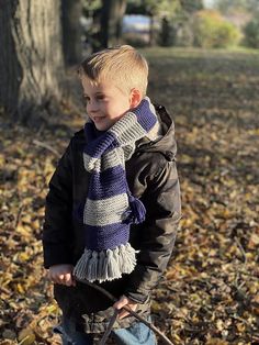 a young boy wearing a scarf standing in leaves