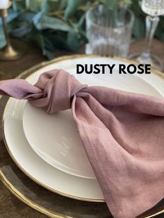 a white plate topped with a pink napkin and gold rimmed place setting on top of a wooden table