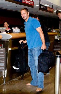 a man in blue shirt and jeans carrying luggage at an air port check in counter