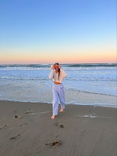 a woman standing on top of a sandy beach next to the ocean with footprints in the sand