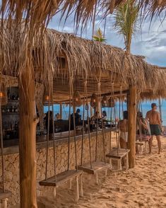 some people are standing on the beach under thatched umbrellas