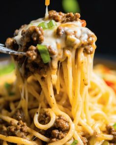 a fork full of spaghetti with ground beef and cheese on top, being lifted from the plate