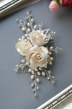 a white rose brooch sitting on top of a table next to a pink flower