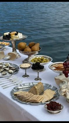 a table topped with lots of different types of food and desserts next to the water