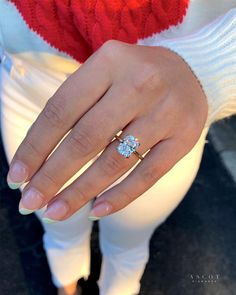 a woman's hand with a diamond ring on her left hand, wearing white pants and a red sweater